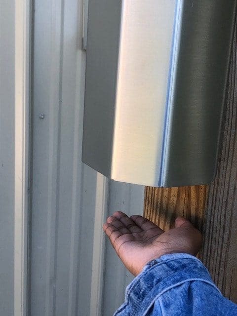 A person reaches their hand beneath a silver hand sanitizer automatic dispenser